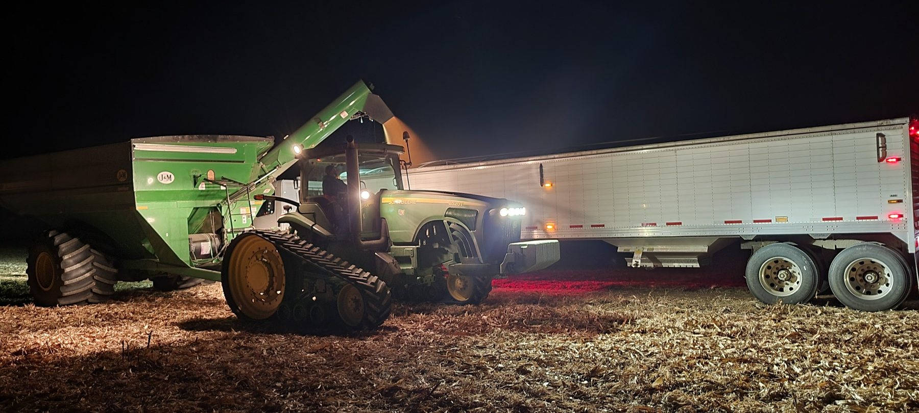Farm tractor, grain cart and semi working after dark during harvest